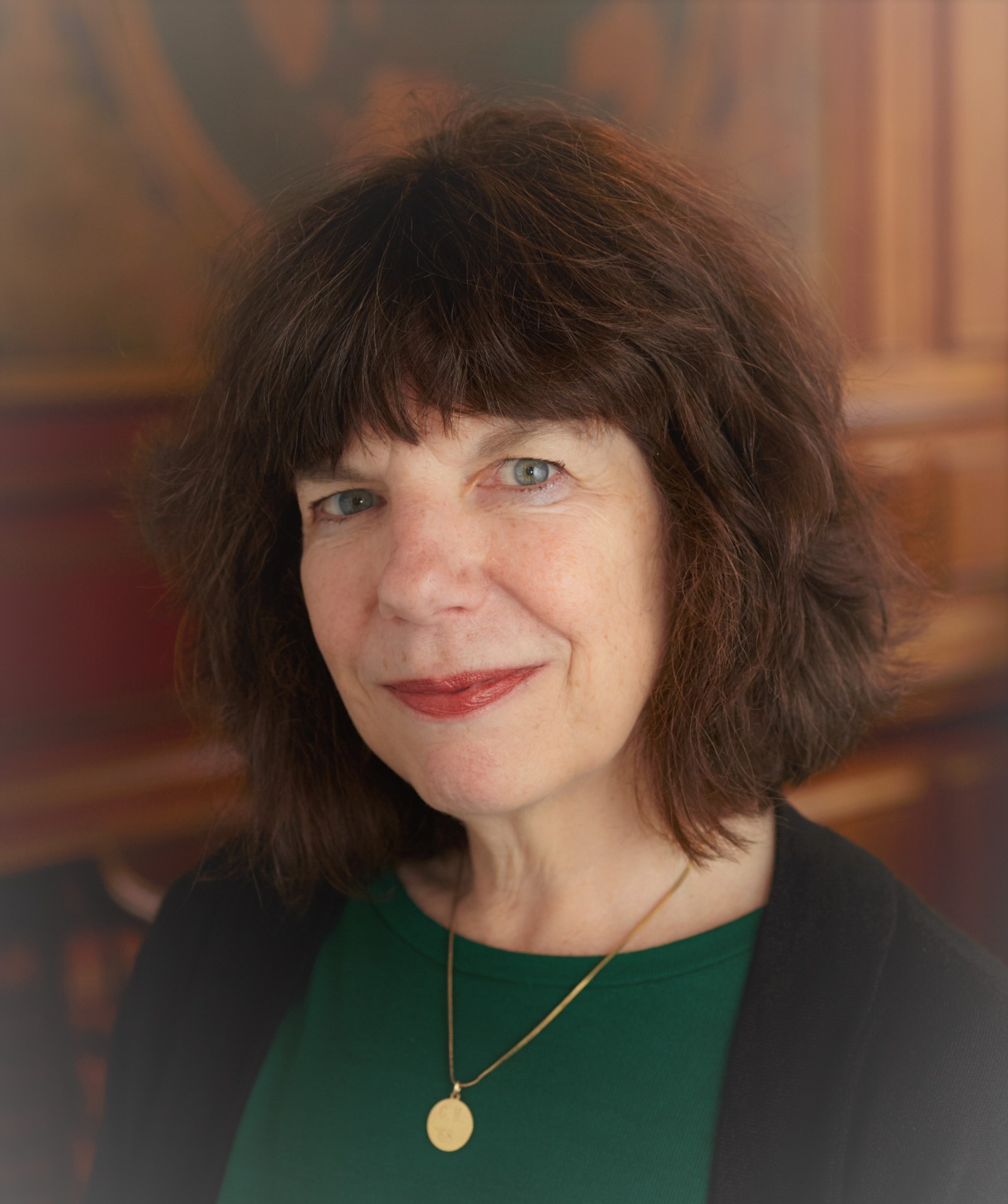 Photo of Peg wearing a green shirt and black wrap. She has short dark hair with bangs. She is wearing a gold necklace.